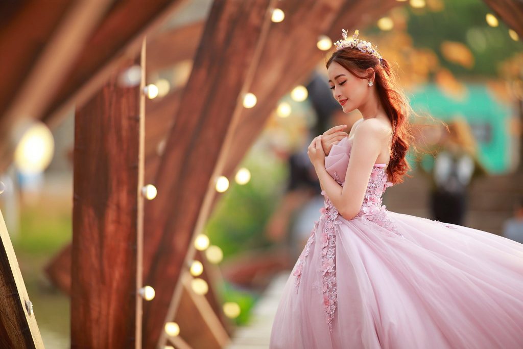 Cô dâu đeo vòng hoa mặc bộ váy cưới màu hồng đằng sau là những ánh đèn lung linh