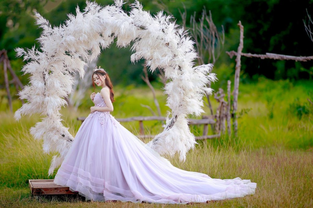Ảnh chụp góc nghiêng cô dâu mặc váy cưới màu tím đứng bên chiếc vòng được gắn đầy lông vũ