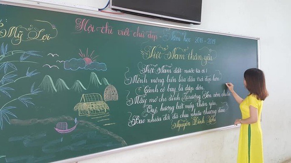 Cô giáo đang viết bài thơ Việt Nam thân yêu lên bảng lên bảng với nét chữ cực đẹp