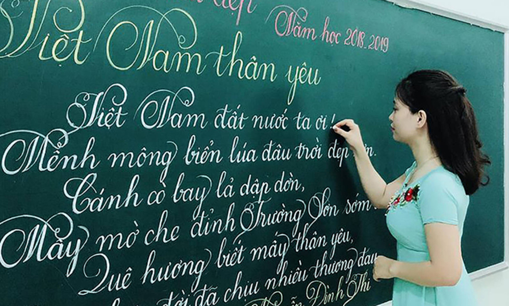 Hình cô giáo đang viết lên bảng bài thơ Việt Nam thân yêu